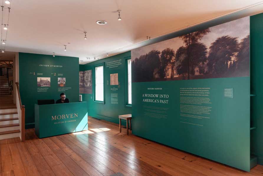 Photo of the Morven orientation gallery, including a seated docent at an information desk, left, and an interpretive wall "A Window Into America's Past," right.