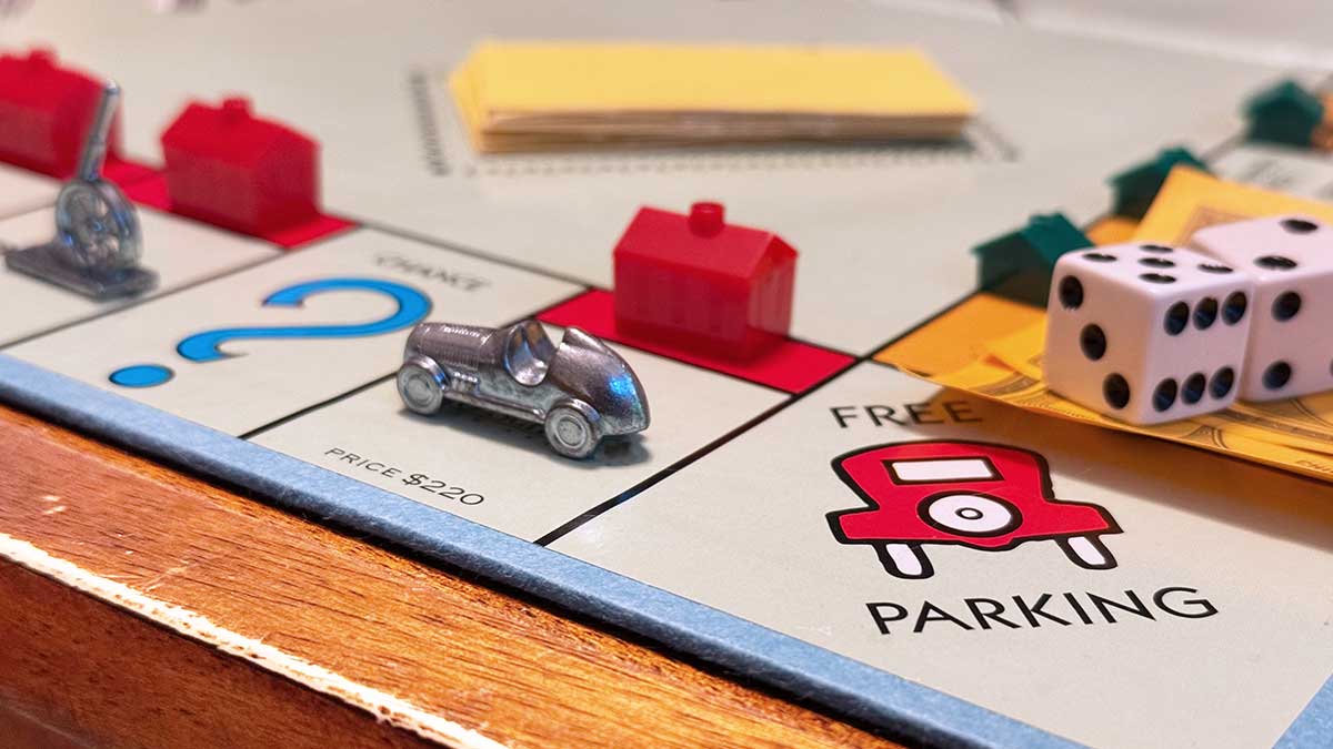 Closeup photo of the spaces around "Free Parking" on a Monopoly Board, with game pieces on various spaces
