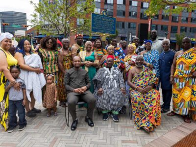Group of about two dozen people, some seated, some standing, in front of the Cudjo Banquante historical marker outside of NJPAC.